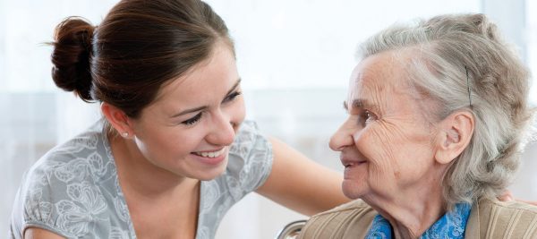 Eine ältere Frau lächelt einer hinter ihr stehenden jungen Frau ins Gesicht