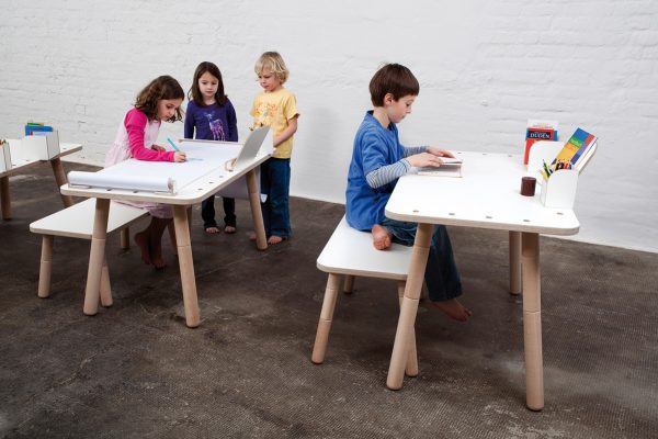 Ein Mädchen malt etwas an einem growing table, ein Junge ließt und zwei weitere Kinder schauen dabei zu