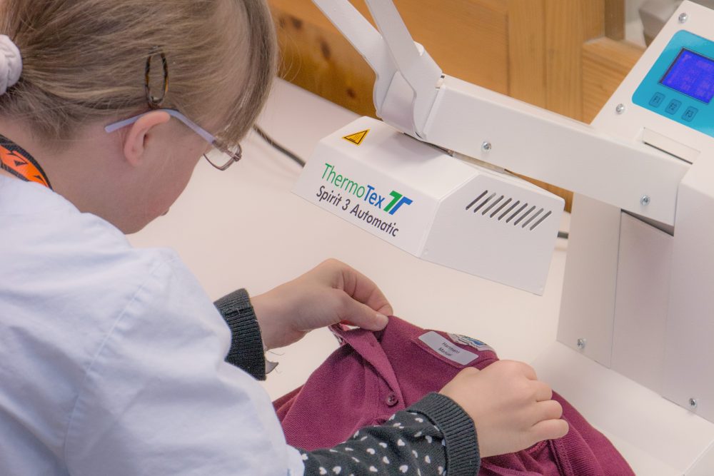 Eine junge Frau näht ein Namensetikett an ein T-Shirt